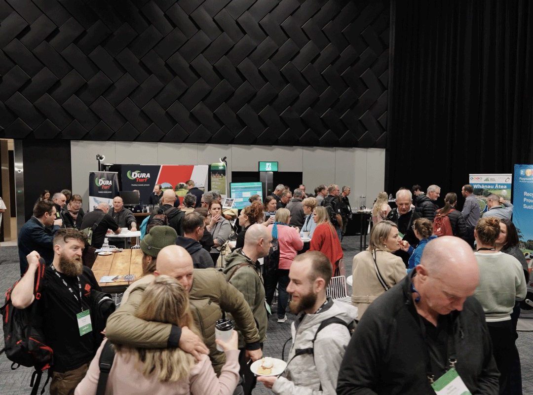 People mingling in a trade booth area, chatting, networking, and exploring displays. The atmosphere is lively and engaging.