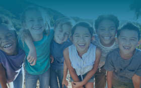 A group of children smile at a camera. A blue filter is overlaid the image