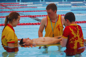 Three lifeguards are in a pool, one is on a floating gurney and the others are helping him. 