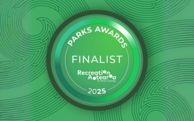 Green button (round shape) with the words Parks Awards 2025 Finalist in white font. The button is overlaid a green patterned background displaying a koru motif