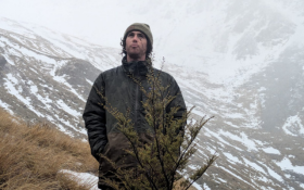 A young man stands on a hilll, there is a mountain behind him